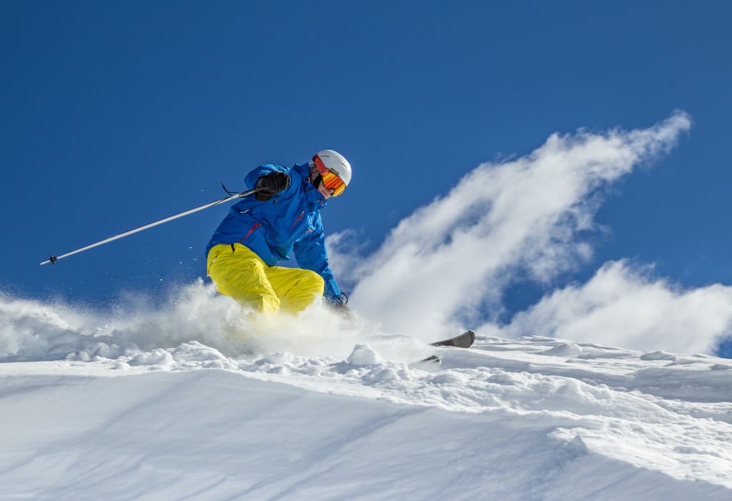 Skier skiing downhill in high mountains during sunny day.