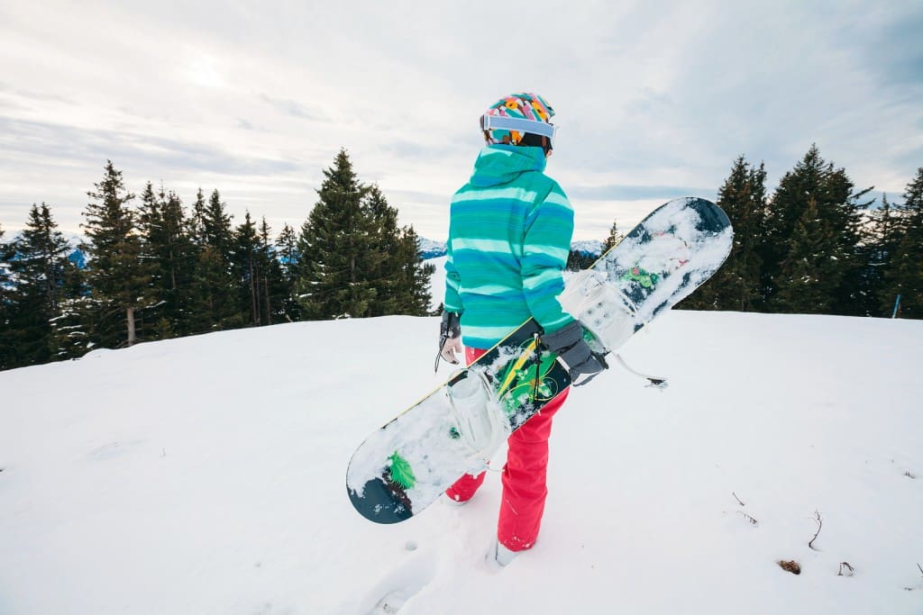 Rear view of female snowboarder with snowboard in hand standing