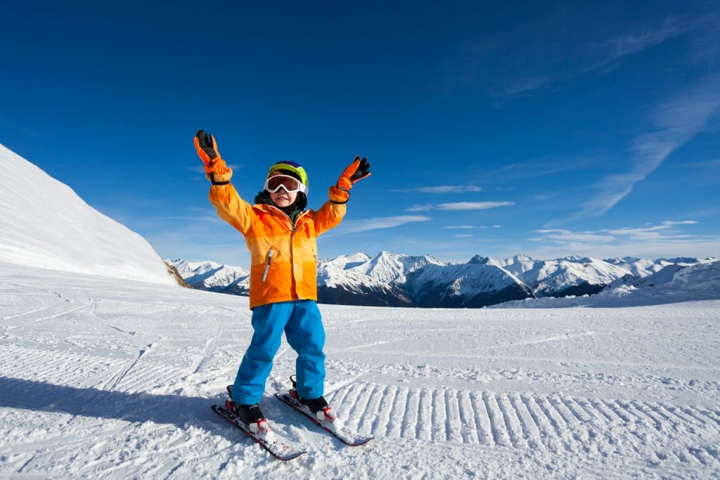 Happy boy with arms up and ski mask on ski-track