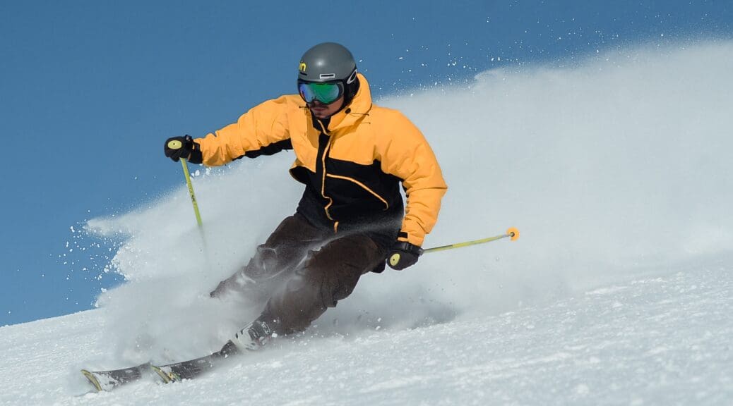 Man skiiing down mountain wearing a yellow and black ski jacket