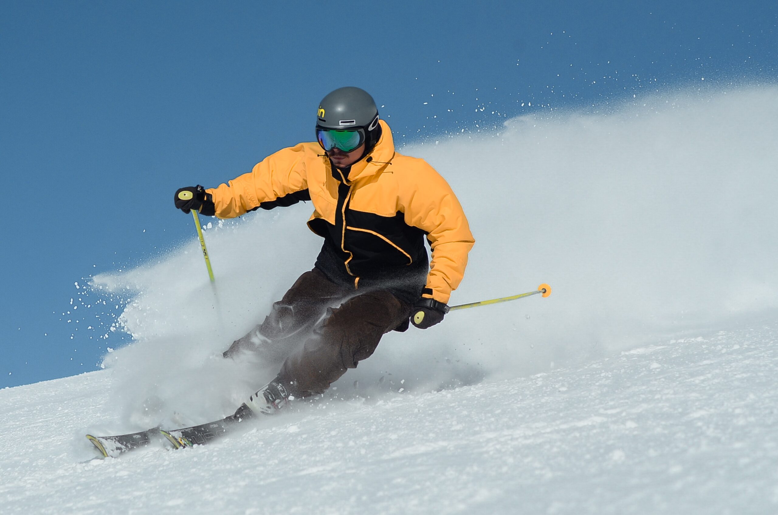 Man skiiing down mountain wearing a yellow and black ski jacket