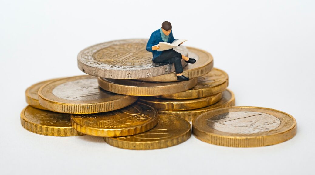 figurine of a man reading a newspaper sat on a stack of euro coins