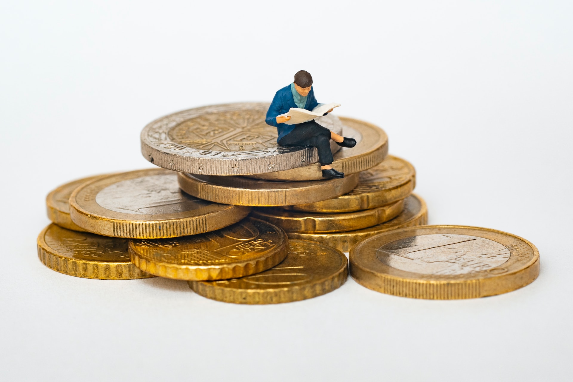 figurine of a man reading a newspaper sat on a stack of euro coins
