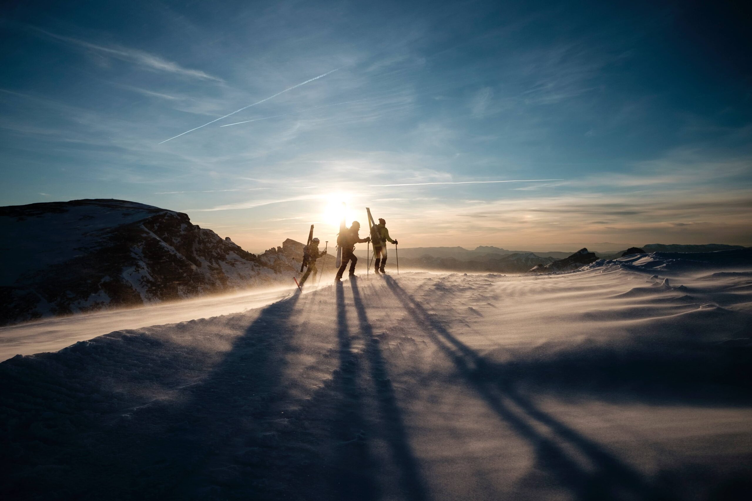 Three young adults skiing on a snowy mountain as the sun begins to go down